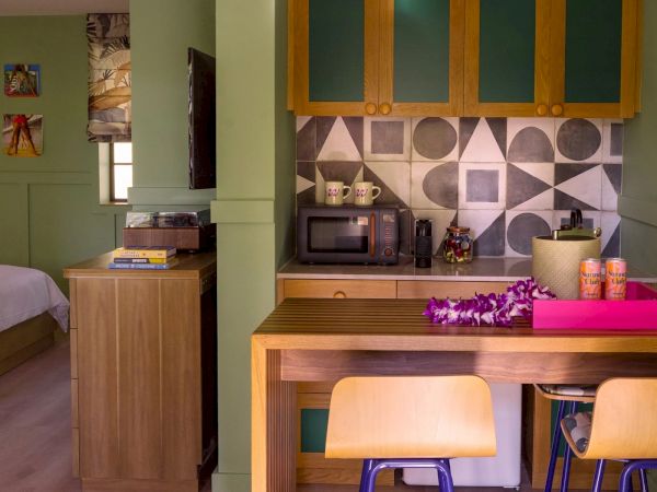 This image shows a cozy kitchen with a microwave, cupboards, and a table setup. There's an adjoining bedroom visible on the left side of the photo.