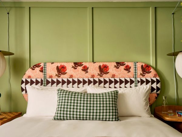 A neatly made bed with floral headboard, checkered pillow, and white pillows; flanked by pendant lights and nightstands with decor and flowers.