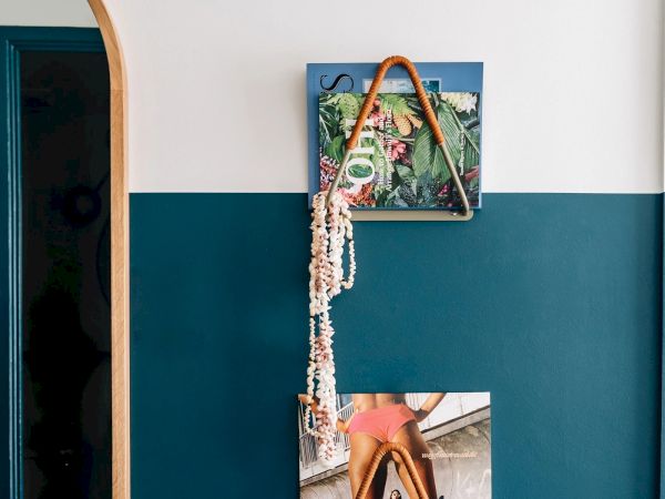 A wall display featuring a framed abstract picture, a triangular rope decoration, a string of seashells, and a partial image of a person on a beach.