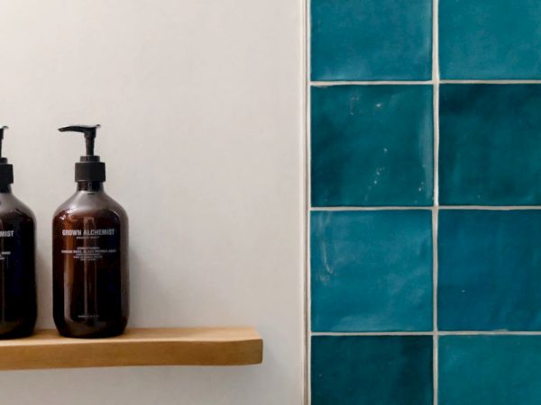 The image shows two pump bottles on a wooden shelf next to a wall with turquoise tiles.