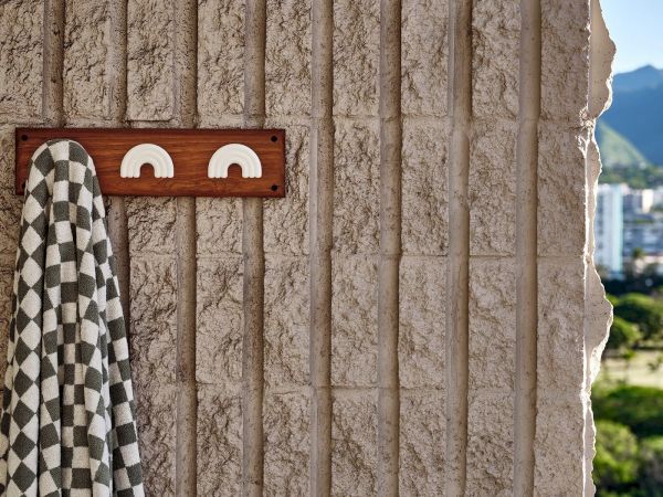 A checkered towel hangs on a textured wall with two rainbow-shaped hooks while a cityscape and mountains can be seen in the background.
