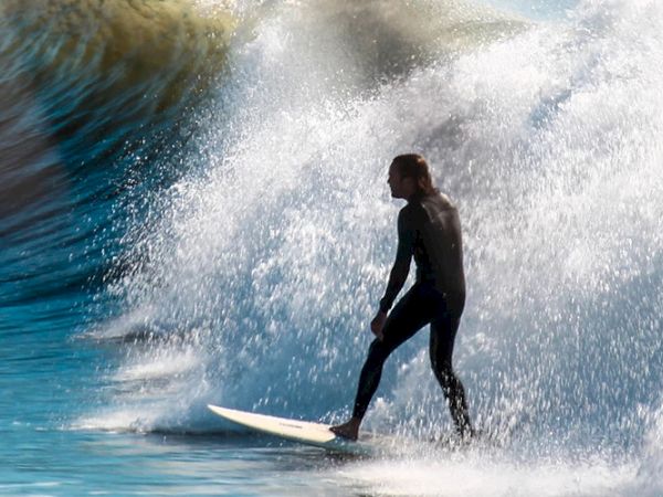 A surfer is riding a wave in the ocean while another person is submerged in the water with just their arm visible, creating a dynamic scene.