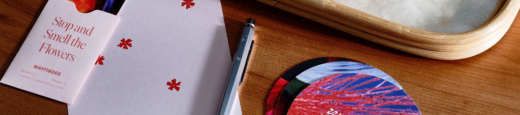 A pen, circular flyers, a notecard with "Stop and Smell the Flowers" text, and a tray on a wooden surface.