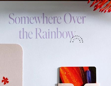The image shows various colorful items including a card that says "Somewhere Over the Rainbow," a plant, and circular objects with vibrant designs.
