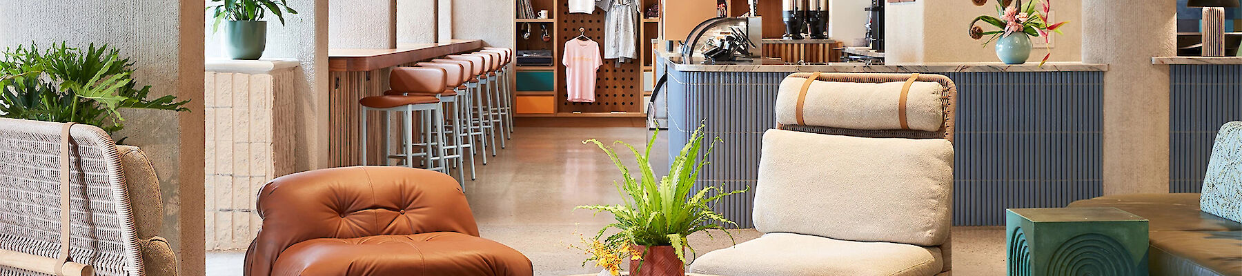 A modern lounge area with various seating options, plants, and a checkered rug, adjacent to a bar with light d&eacute;cor and displayed merchandise.