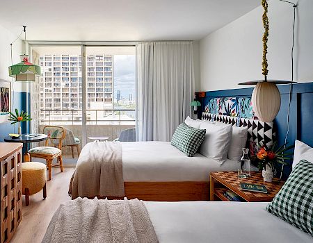 A cozy hotel room with two beds, a balcony, vibrant decor, and city view. end of sentence.