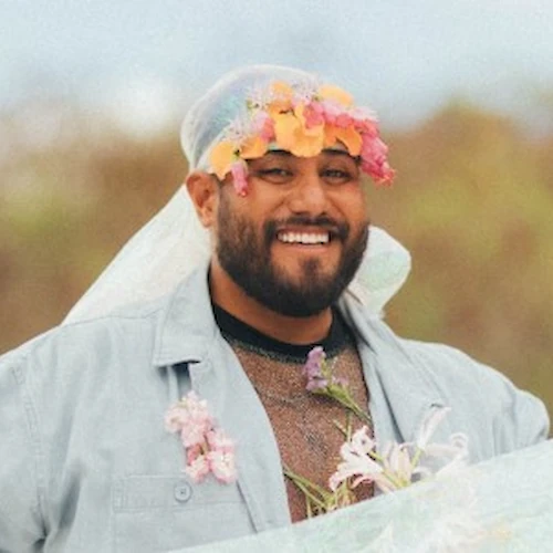 Eine Person steht im Freien, l&auml;chelt und tr&auml;gt einen Blumenkranz und einen hauchzarten Schleier. Der Hintergrund ist verschwommen und nat&uuml;rlich.