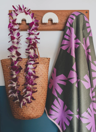 Un perchero decorativo con adornos coloridos y un collar de flores colgando, una camisa tropical colgada y un bolso tejido.