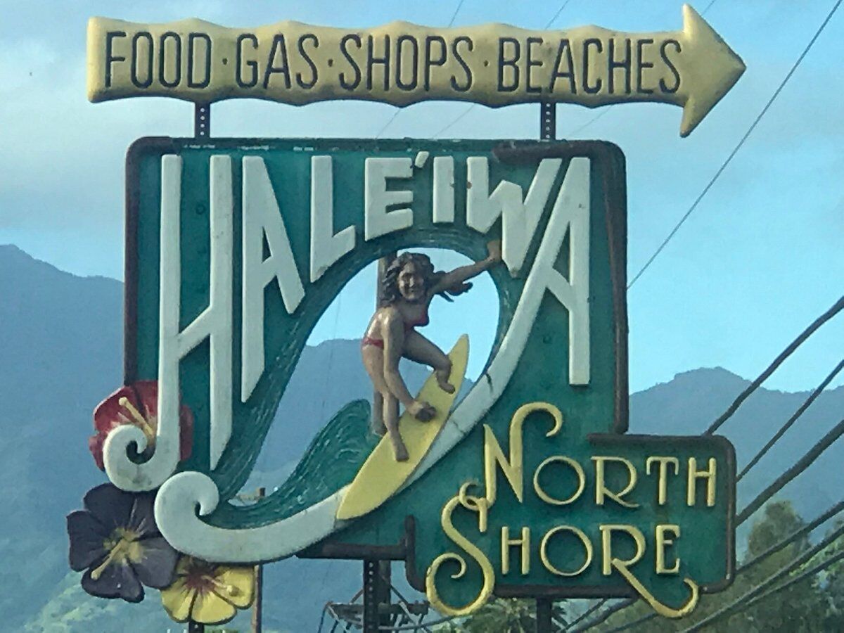 A sign saying "Haleiwa North Shore" with a surfer illustration, and a directional arrow labeled "Food, Gas, Shops, Beaches."