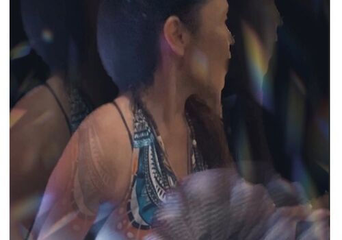 A person wearing a white and blue outfit is holding a decorative fan. The image has a blurred, ethereal effect.