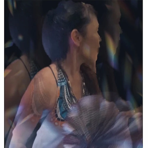 A person wearing a white and blue outfit is holding a decorative fan. The image has a blurred, ethereal effect.