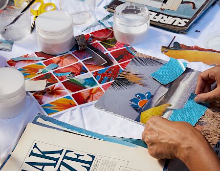 Three people working on a collage with various materials, such as magazines, paper, scissors, and glue, on a table.