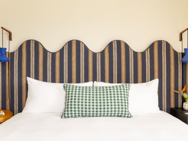 The image features a bed with white pillows, a green checkered cushion, a colorful wavy headboard, and blue bedside lamps.