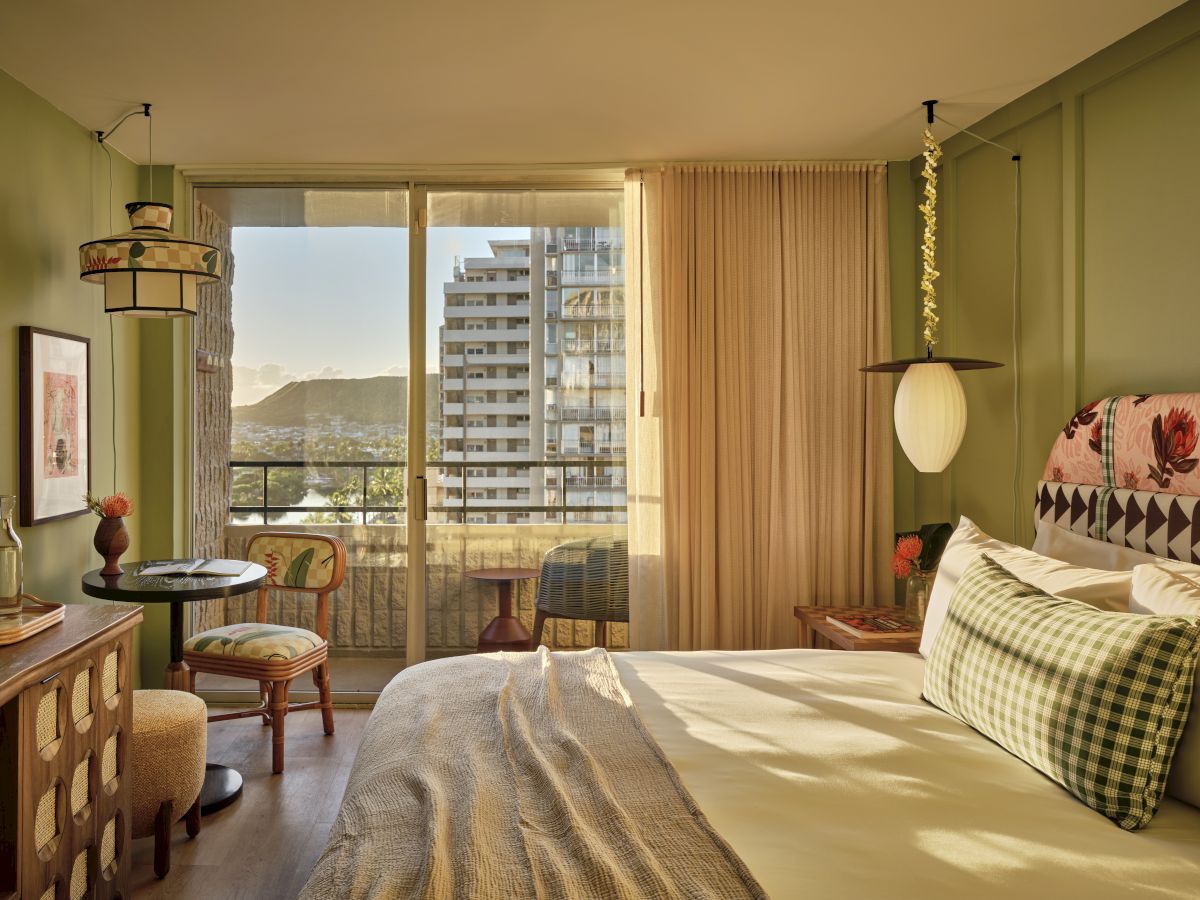 A bright hotel room with a large window view of buildings and hills, olive walls, a bed with green plaid pillows, and a round desk chair setup, ending the sentence.