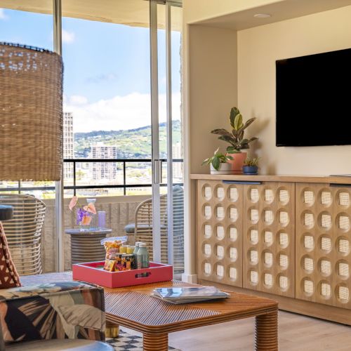 Ein gem&uuml;tliches Wohnzimmer mit Fernseher, Schrank, Pflanze und Blick auf die Terrasse. Korbm&ouml;bel und ein geflochtener Lampenschirm sorgen f&uuml;r eine nat&uuml;rliche Note.