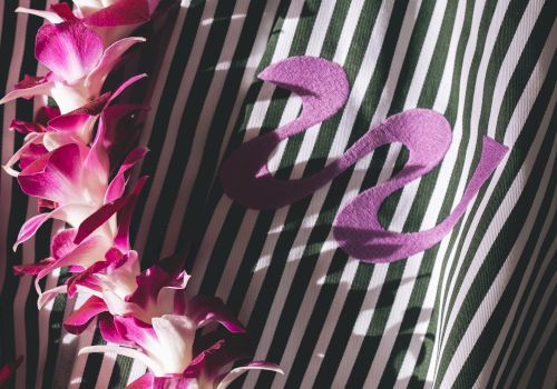 A strand of pink-purple flowers drapes over a striped black-and-white fabric with a cursive &ldquo;z&rdquo; emblem, creating a tropical, elegant contrast.