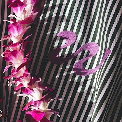 A strand of pink-purple flowers drapes over a striped black-and-white fabric with a cursive &ldquo;z&rdquo; emblem, creating a tropical, elegant contrast.