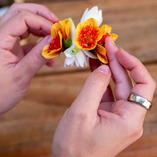 Hands gently hold a small bouquet of orange and white flowers, like marigolds and daisies.