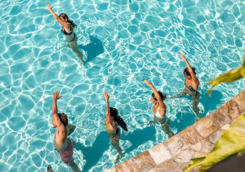 Five people are exercising in a swimming pool, performing synchronized movements near the pool's edge.