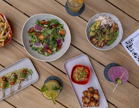 An assortment of dishes on a table, including salads, fries, skewers, and drinks, alongside a visible menu on the top right.