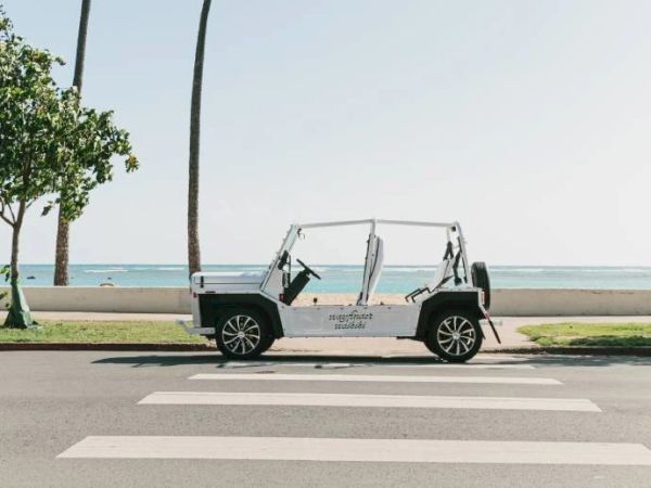 An open-top vehicle is parked beside a beach, with palm trees and the ocean in the background, near a pedestrian crosswalk.