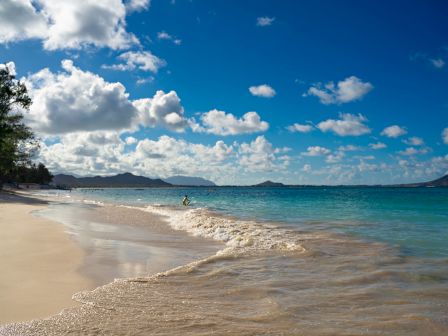 A sunny tropical beach with clear turquoise water, white sand, and fluffy clouds in a bright blue sky, peaceful and inviting.