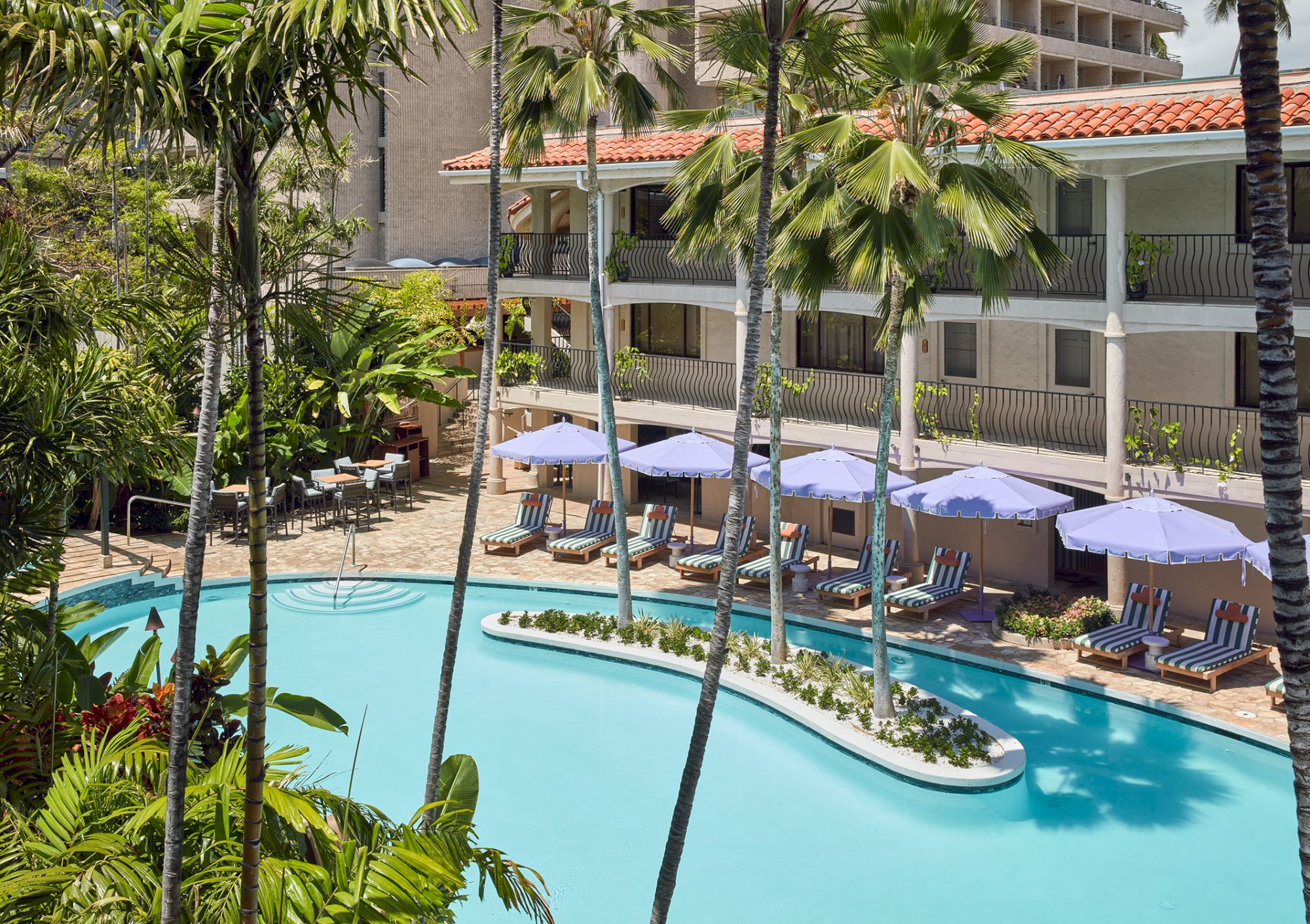 A sunny resort pool with palm trees, lounge chairs, and shaded cabanas around a curved blue pool, inviting relaxation and tropical vibes.