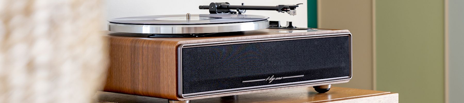 木製のレコードプレーヤー／ターンテーブルが装飾的なキャビネットの上に置かれ、その上には色鮮やかな壁掛けアートが飾られている。