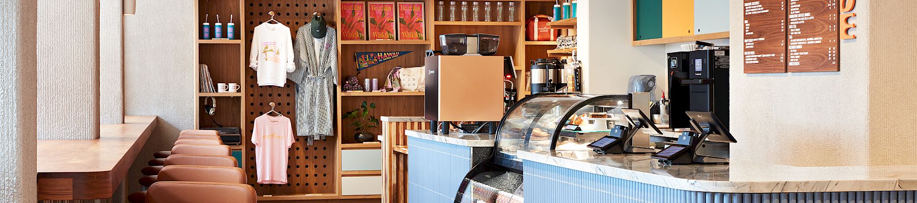 A modern caf&eacute; interior with a glass display counter, espresso machines, menu boards, and sleek ceiling fans overhead.