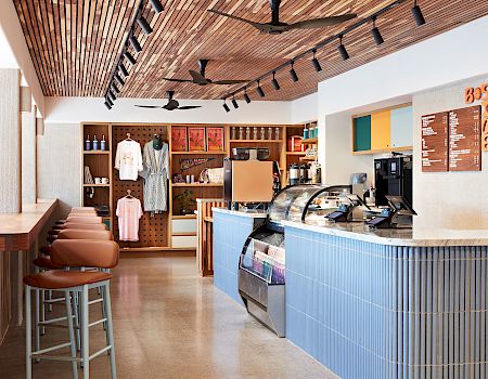 Un interior de cafetería moderno con mostrador de cristal, máquinas de espresso, pizarras con el menú y elegantes ventiladores de techo.