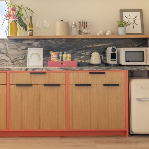 Eine moderne K&uuml;chentheke mit Steinr&uuml;ckwand, Blumen, Weinflaschen, Gl&auml;sern, einer Kaffeemaschine und einem Sp&uuml;ltischhahn.