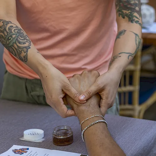 Two tattooed people hold hands and shape a heart, showing affection in a casual outdoor caf&eacute; setting.