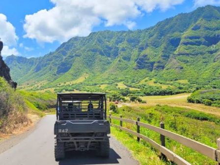 Un cami&oacute;n de estilo militar circula por una carretera asfaltada que atraviesa un valle verde y exuberante, con imponentes monta&ntilde;as y un cielo azul en lo alto.