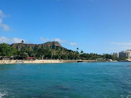 Una playa tropical con aguas turquesas, palmeras, un paisaje monta&ntilde;oso de fondo y hoteles a lo largo de la costa.