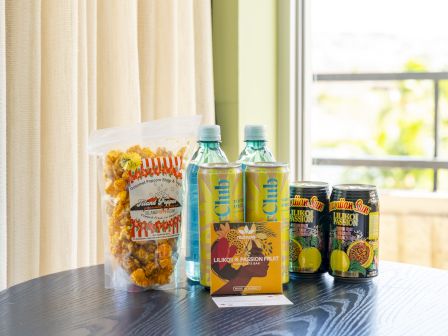 A table of Hawaiian treats: popcorn, drink bottles, Hawaiian Sun Likiloki Passion cans, and a Liliko&rsquo;i x Passion chocolate bar.