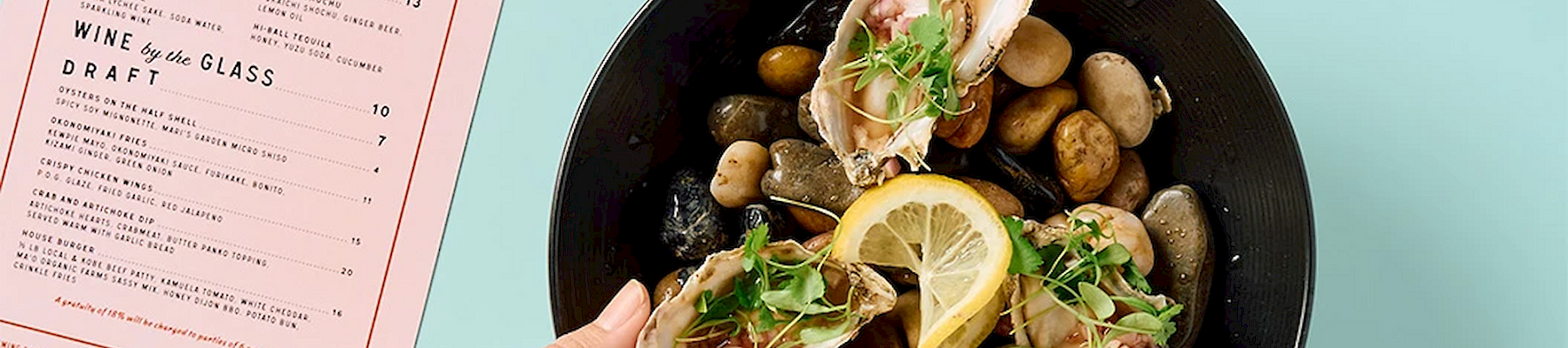 A hand points at a plate of oysters and lemony seafood with a &ldquo;Redfish&rdquo; happy-hour menu card beside it.